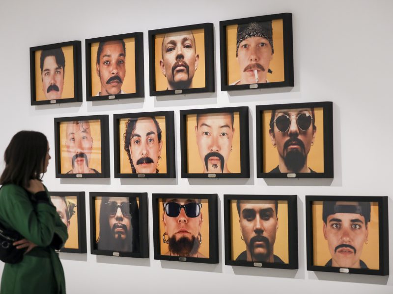 Person looking at an photography exhibition of portraits all with moustaches and facial hair.