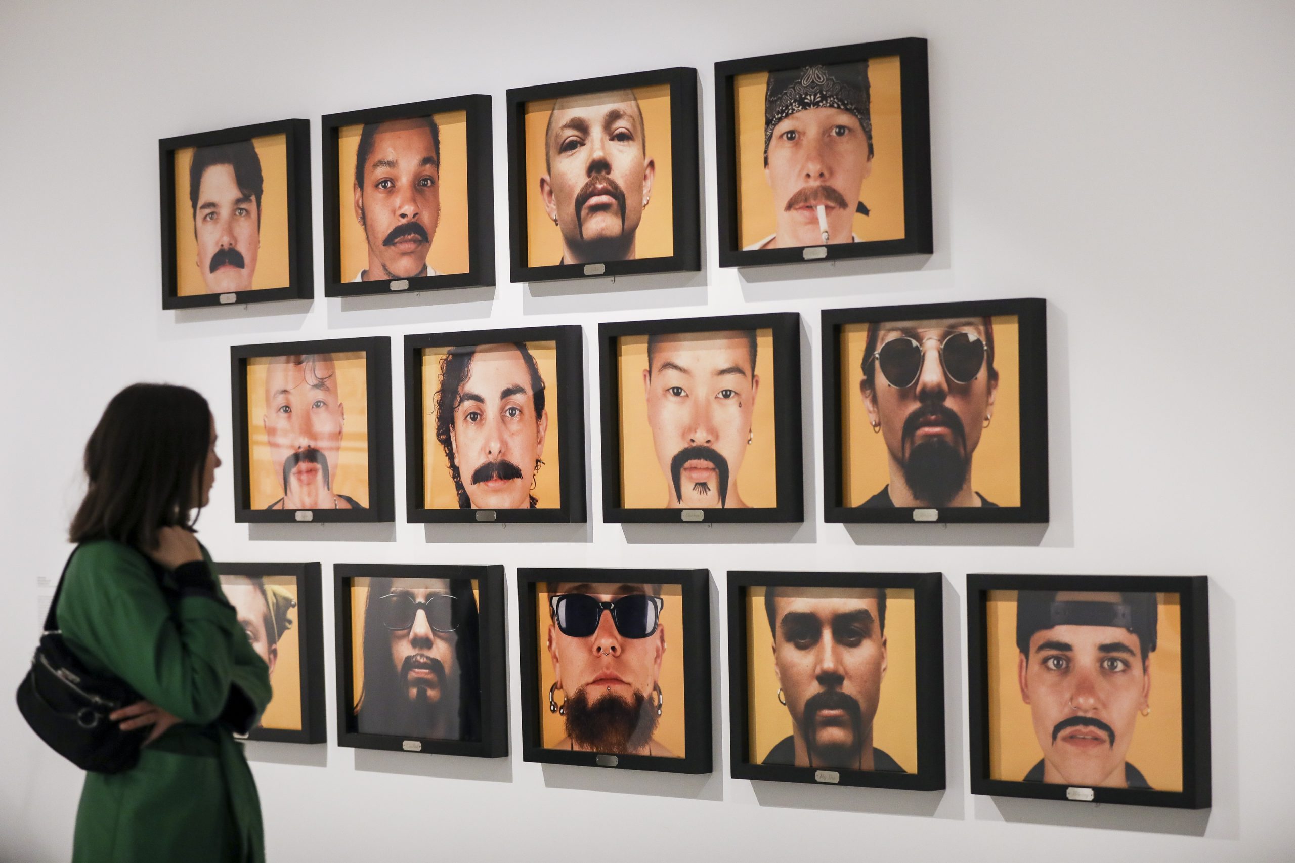 Person looking at an photography exhibition of portraits all with moustaches and facial hair.