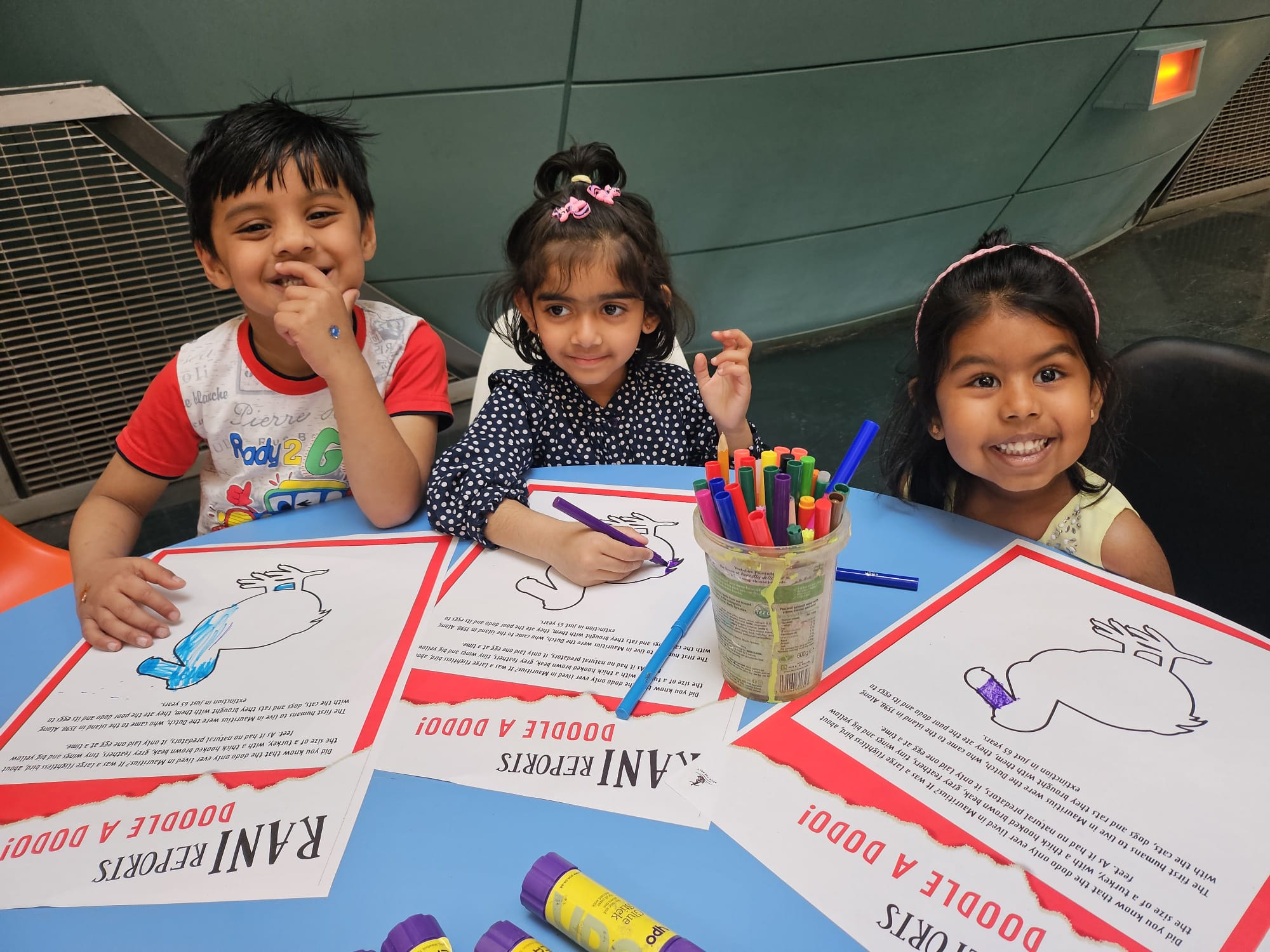 Three children drawing and smiling at the camera