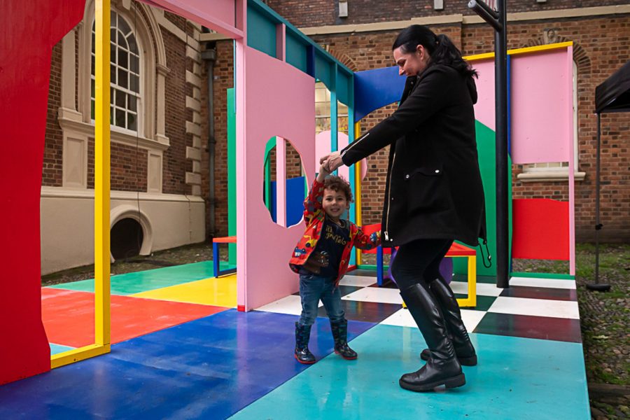 A child and adult holding hands and dancing on a colour stage and installation