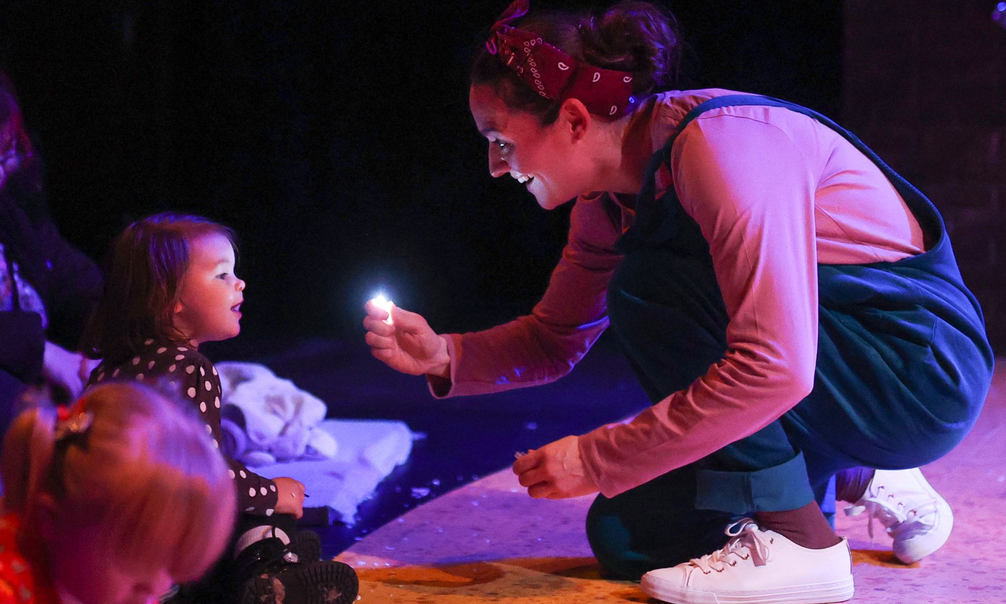 Adult holding a small light towards a child, and illuminating their face