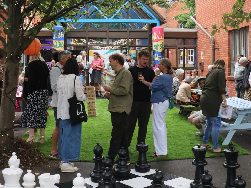 A gathering in an outside space with a giant chessboard in the foreground