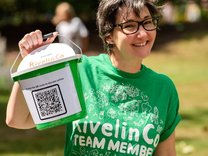 A RivelinCo team member holding up a donation bucket with a QR code on the front