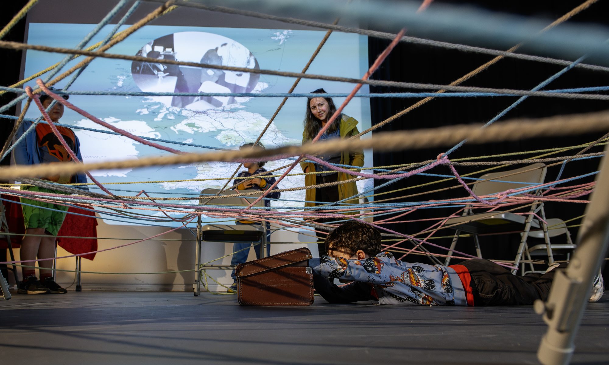 A child peers into a suitcase, under a web of colourful string