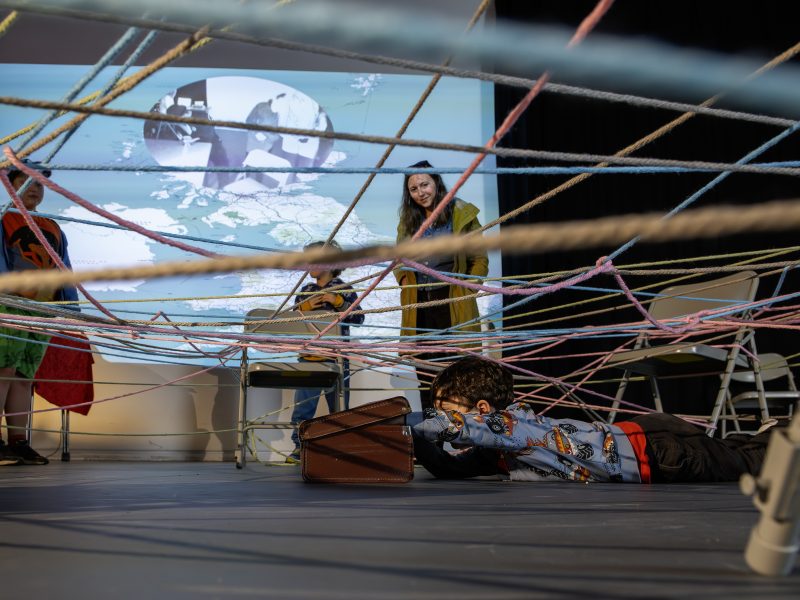 A child peers into a suitcase, under a web of colourful string