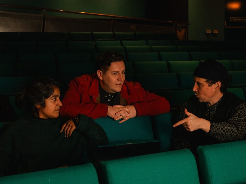 Three people chatting, seated in cinema seats.